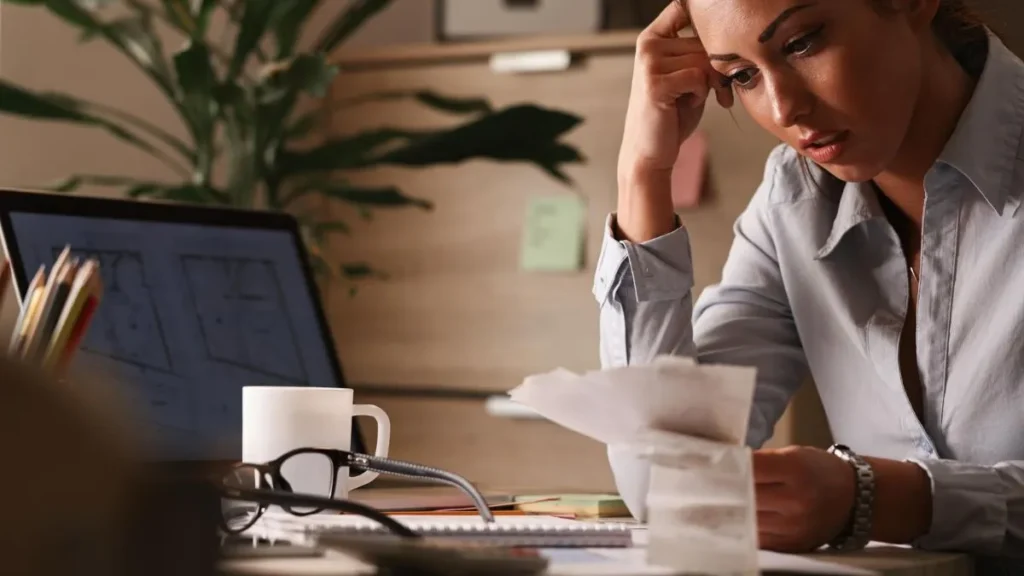 Pessoa estressada com contas e documentos financeiros na mesa.